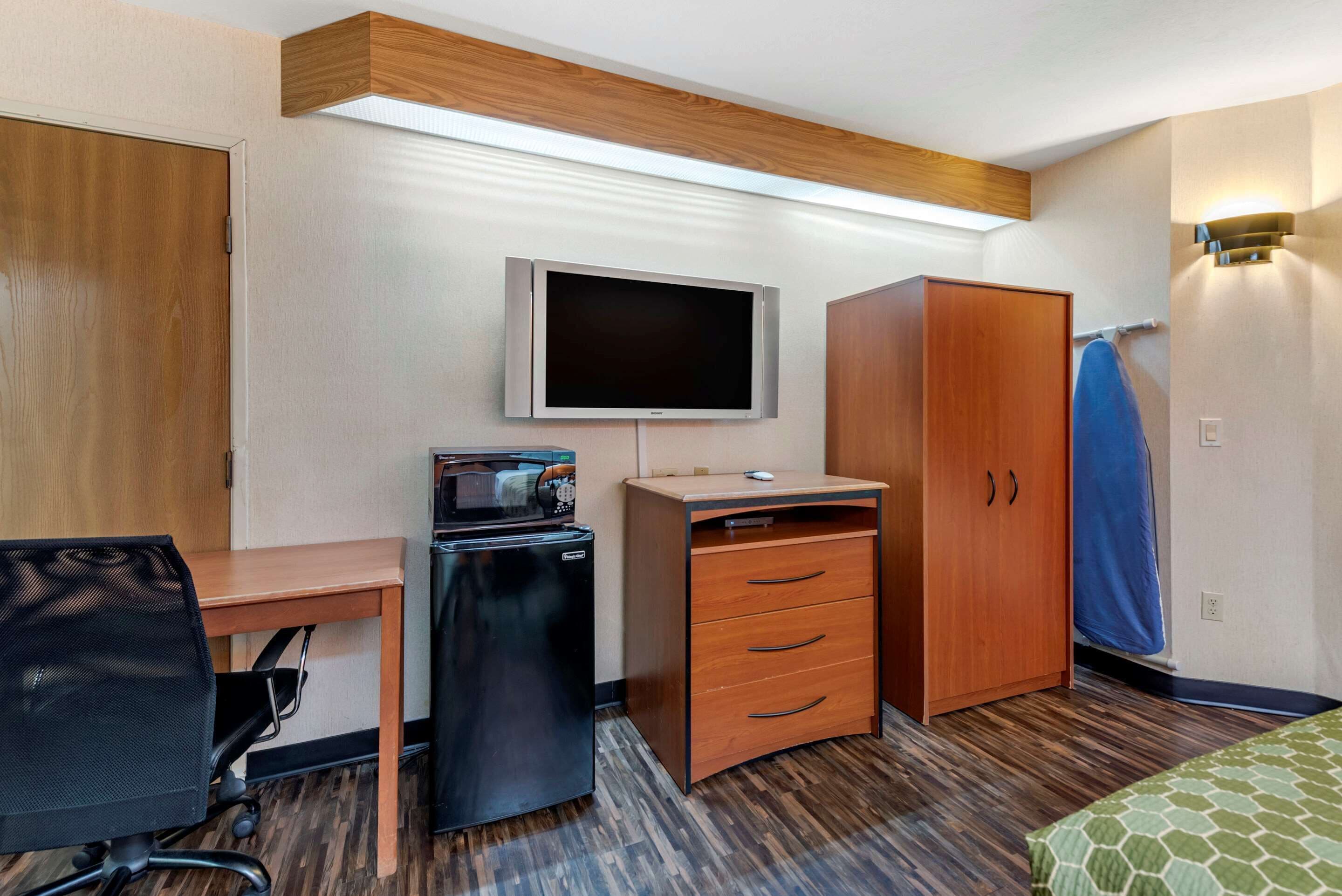 Una habitación de hotel con un escritorio de madera, televisión, armario y microondas.