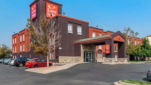 A hotel with a brown exterior, a red car parked in front, and a clear blue sky. - Econo Lodge North Academy (Colorado Springs)