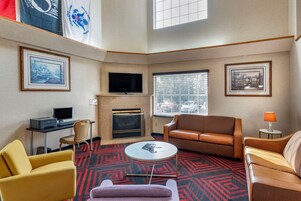 Una habitación de hotel con chimenea, televisor, escritorio con ordenador y dos sofás.
