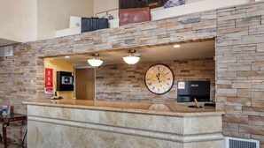 A reception area with a stone wall, a clock, a television, and a counter. - Econo Lodge North Academy (Colorado Springs)