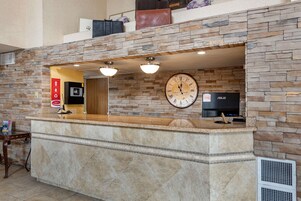 Un área de recepción con pared de piedra, un reloj, un televisor y una barra de recepción.