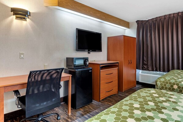 Habitación de hotel con escritorio, silla, televisión, microondas, armario y cama.