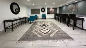 A spacious room with a long bench, a blue chair, a patterned rug, and a kitchen area with bar stools.
