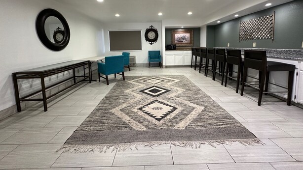 A spacious room with a long bench, a blue chair, a patterned rug, and a kitchen area with bar stools.