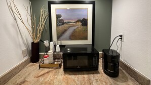 A kitchen area with a framed painting, a microwave, a coffee maker, and a sugar container on the counter.