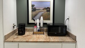 A kitchen counter with a coffee maker, a microwave, and a stack of white cups.