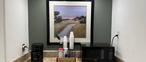 A kitchen counter with a coffee maker, a microwave, and a stack of white cups.