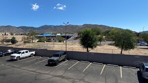 A parking lot with several vehicles, a building with a blue roof, and mountains in the background.