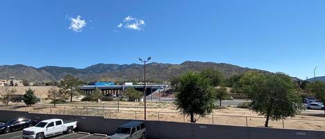 A parking lot with several vehicles, a building with a blue roof, and mountains in the background.