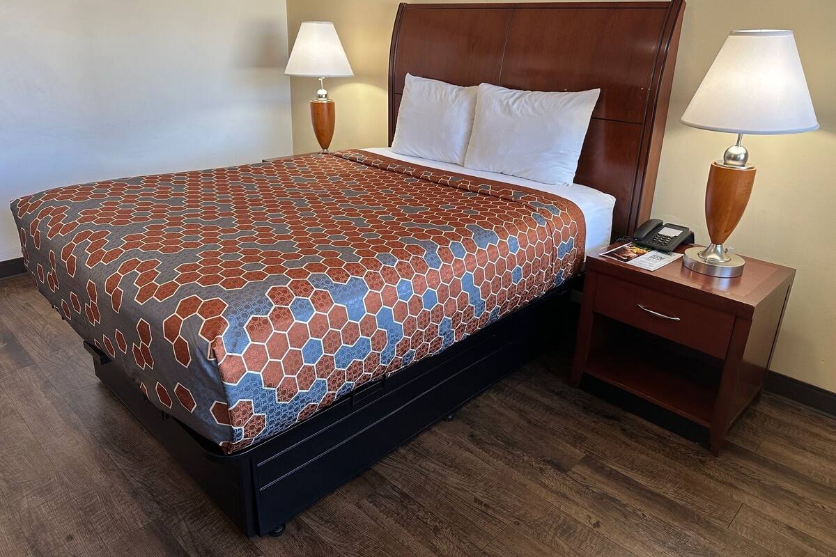 A hotel room with a bed, two bedside lamps, a wooden nightstand, and a wooden floor.