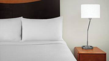 A neatly made bed with white linens and a wooden headboard, a bedside table with a lamp, and a drawer.