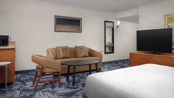 A hotel room with a bed, a sofa, a small table, a TV, and a mirror.