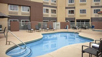 A swimming pool with lounge chairs and a fence, surrounded by a multi-story building with balconies.