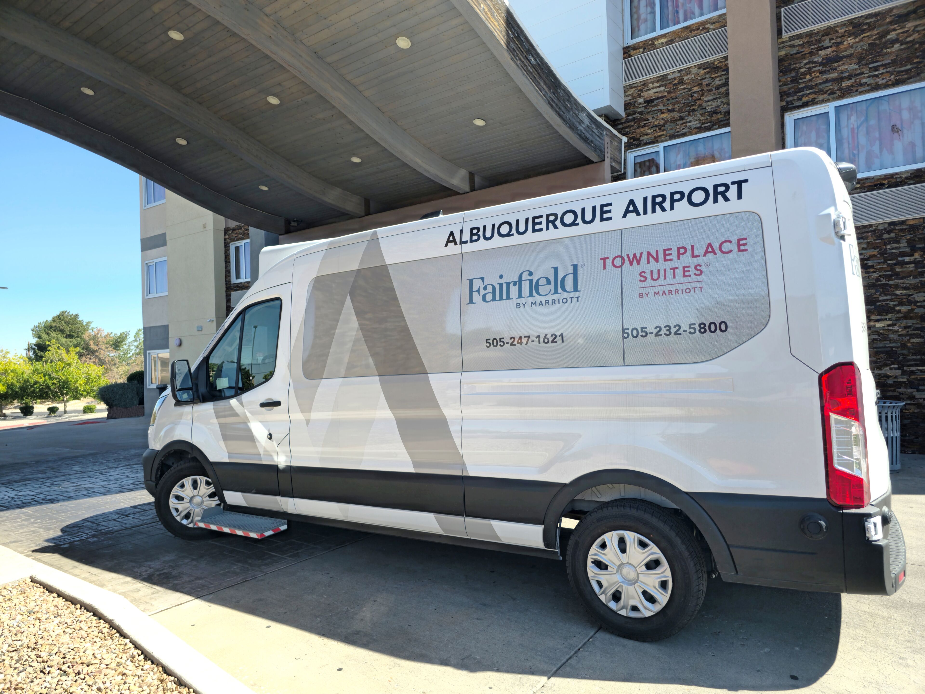 Una camioneta blanca estacionada bajo un edificio con la leyenda 'Albuquerque Airport' y 'Fairfield by Marriott' en su lateral.