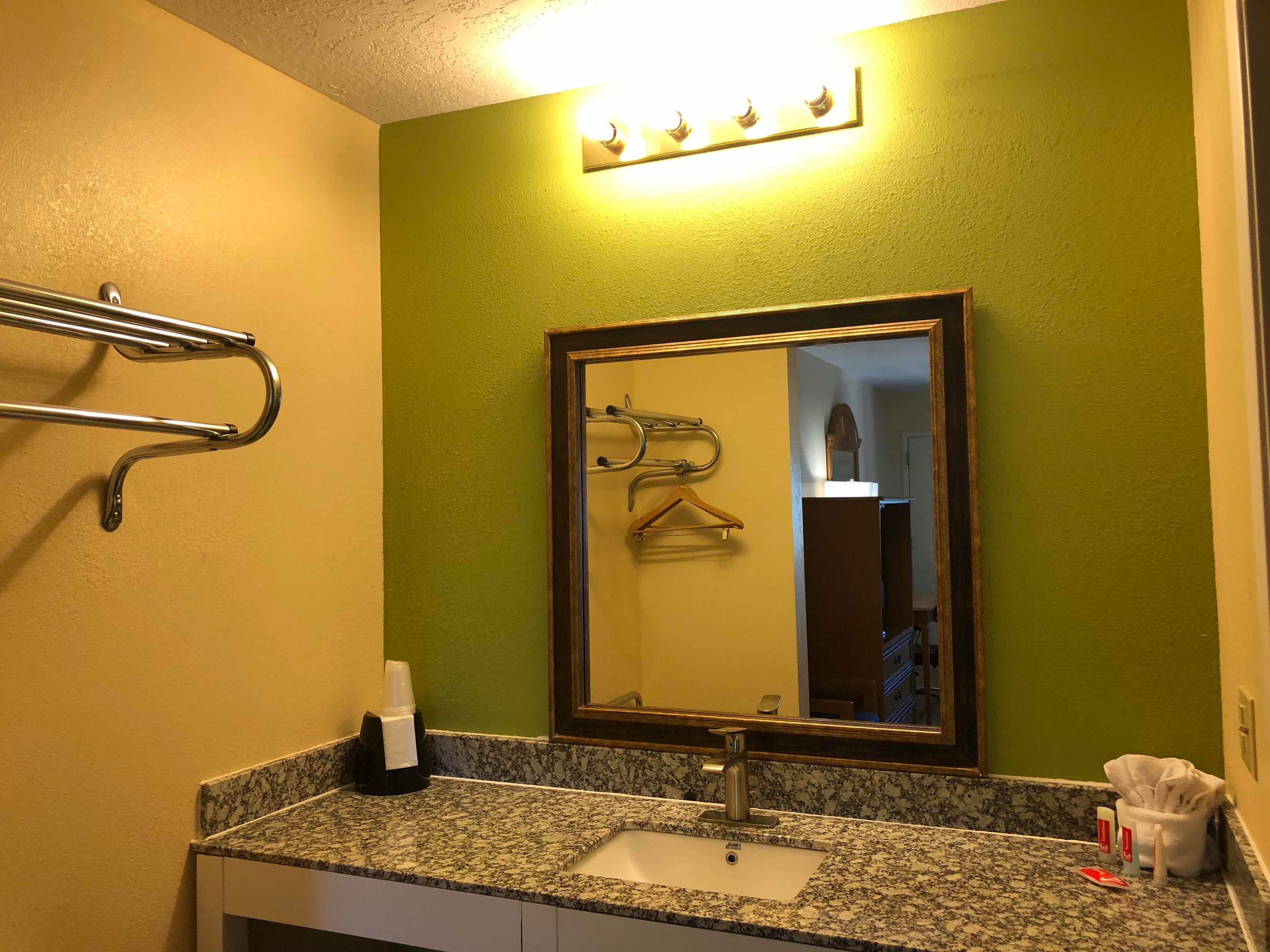 A bathroom with a granite countertop, a sink, a mirror, and a towel rack.