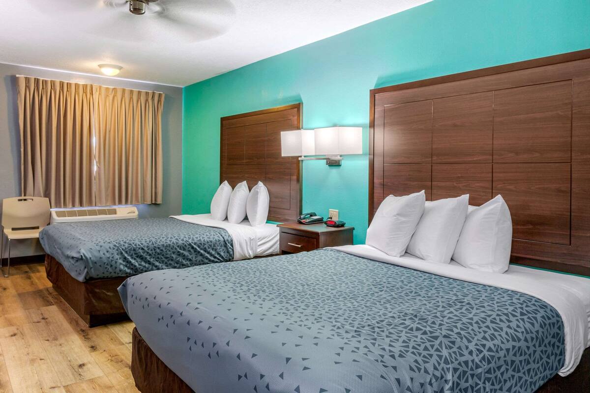 Habitación de hotel con dos camas, un escritorio, una silla, una lámpara y una ventana con cortinas.