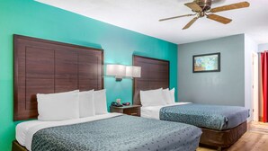 A hotel room with two beds, teal walls, wooden headboards, a ceiling fan, and a nightstand with a lamp. - Econo Lodge West - Coors Blvd (Albuquerque)