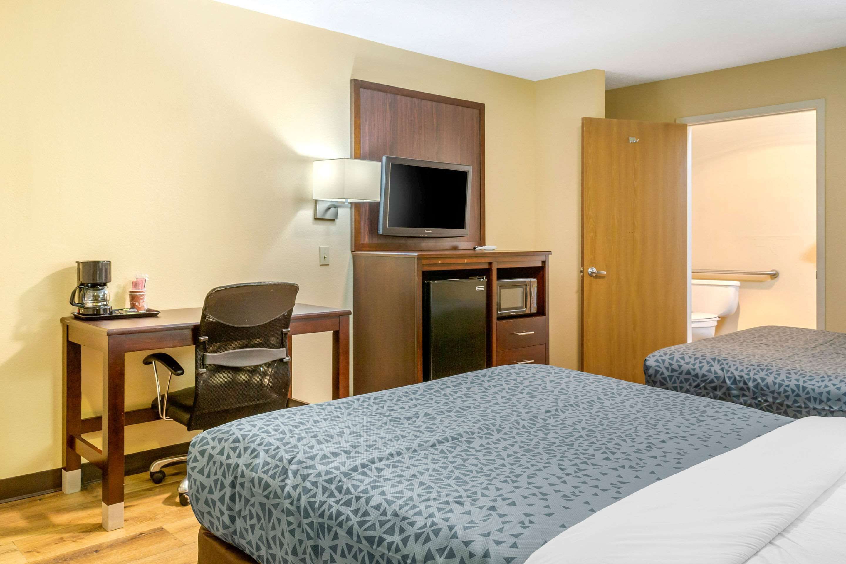 A hotel room with a desk, chair, television, and two beds.