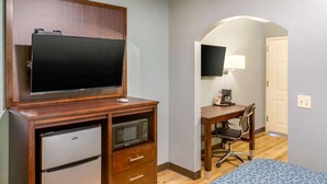 A compact room with a wooden desk, a television mounted above it, a microwave, a refrigerator, a chair, and a bed with a patterned cover. - Econo Lodge West - Coors Blvd (Albuquerque)