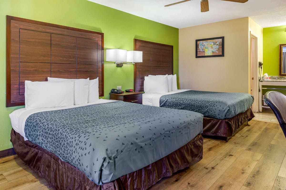 Habitación de hotel con dos camas, una mesita de noche, una lámpara y un cuadro en la pared.