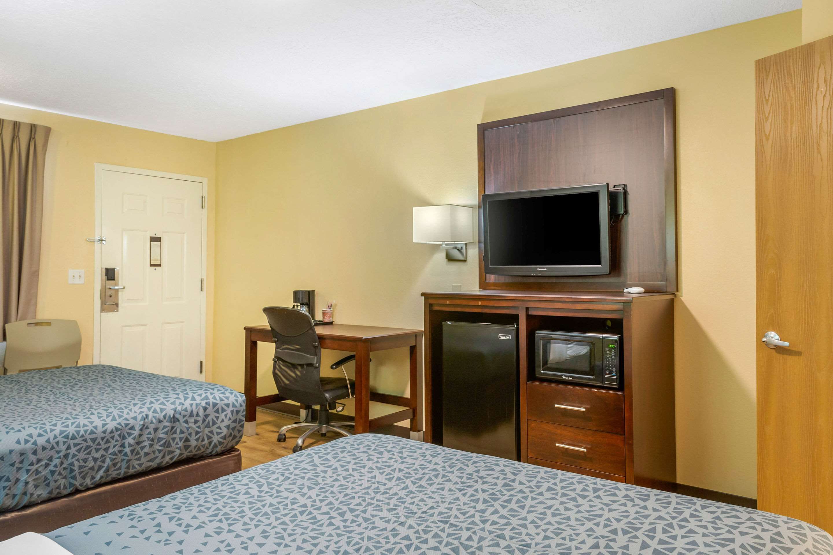 A hotel room with two beds, a desk, a television, a refrigerator, and a microwave.