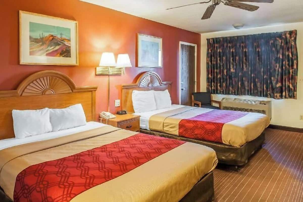 Habitación de hotel con dos camas, un ventilador de techo, una mesita de noche con lámpara y una ventana con cortinas.
