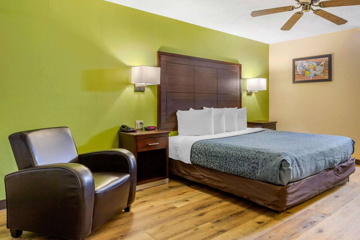 Habitación de hotel con cama, una silla, una mesita de noche y un ventilador de techo.