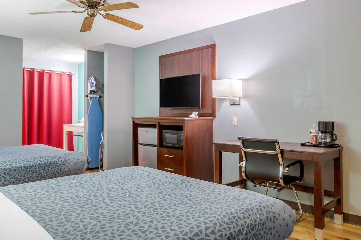 Habitación de hotel con dos camas, un escritorio, una silla, un televisor, un microondas y un ventilador de techo.