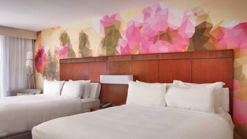 Een hotelkamer met twee bedden, een houten hoofdbord, een wand met een geometrisch bloemenpatroon en een nachtkastje met een lamp.