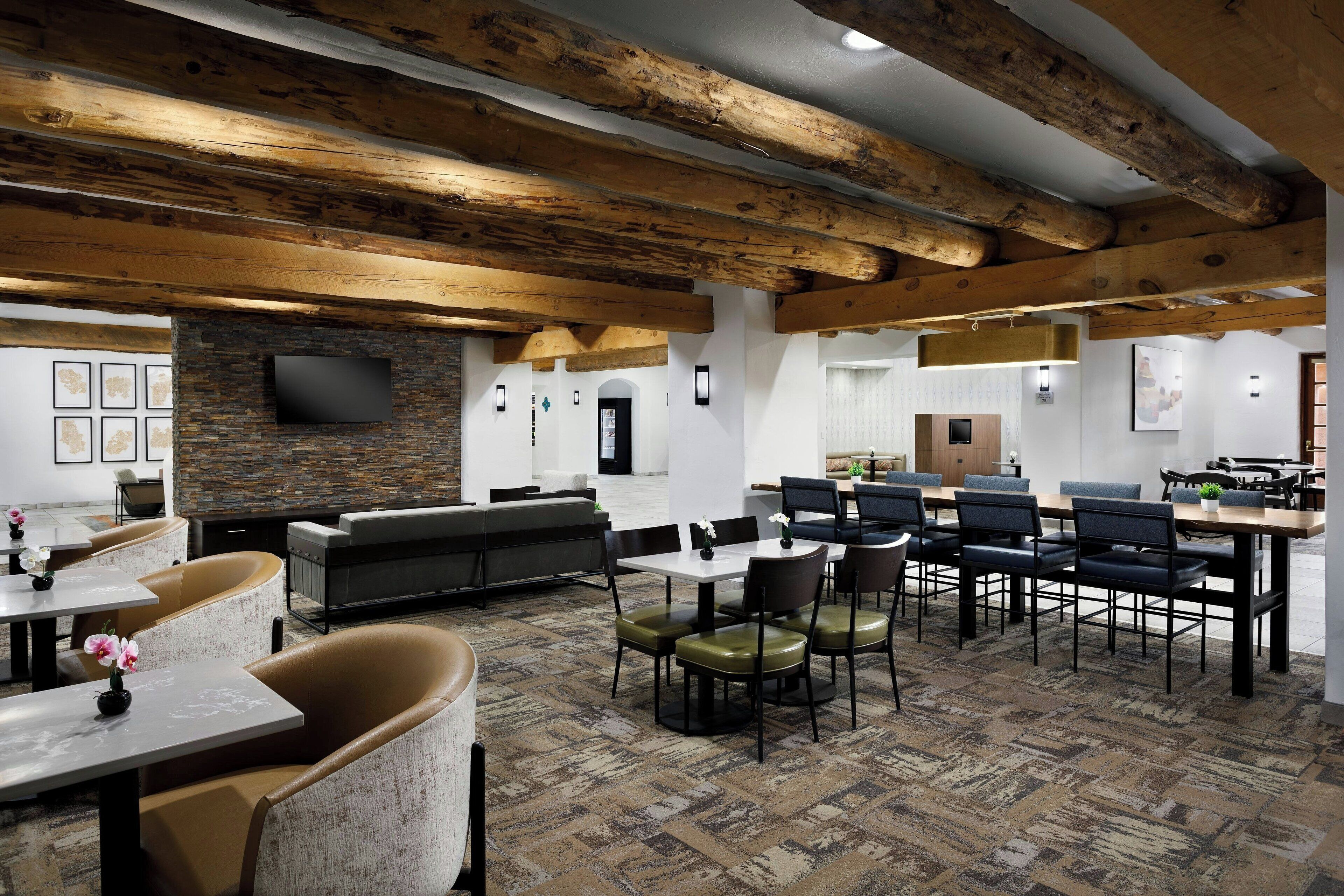 A spacious indoor area with a high ceiling supported by exposed wooden beams, a stone fireplace, and a flat-screen TV mounted on the wall.
