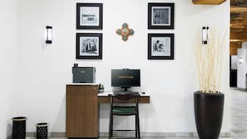A reception desk with a computer, framed pictures on the wall, a decorative wall piece, and a tall vase with branches.