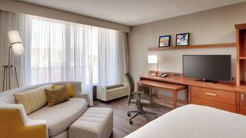 A hotel room with a sofa, a desk, a television, and a bed.