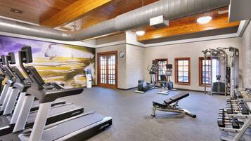 A gym with treadmills, weight machines, and a mural on the wall.