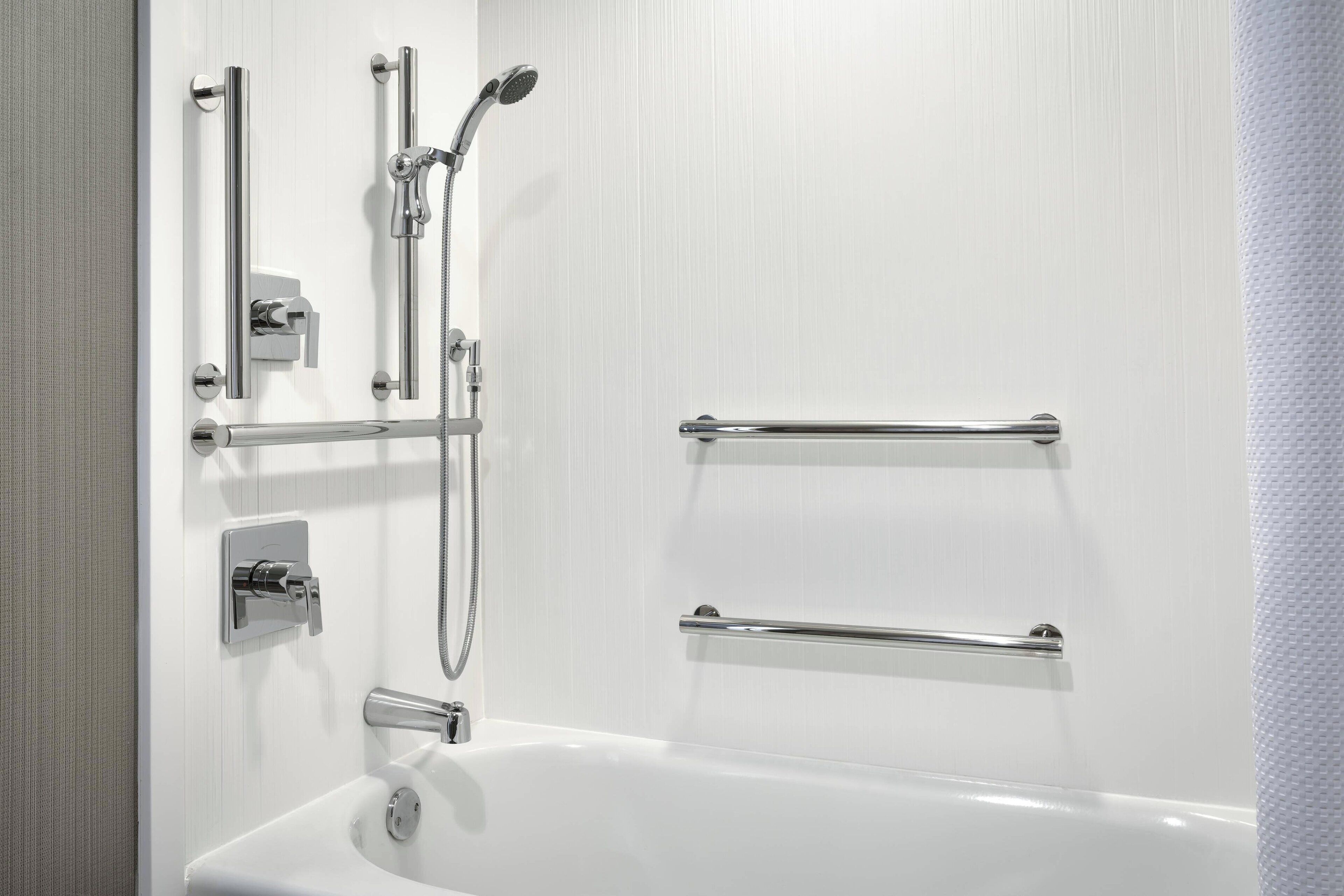 Ein modernes Badezimmer mit einer weißen Badewanne, Chromarmaturen und Haltegriffen.