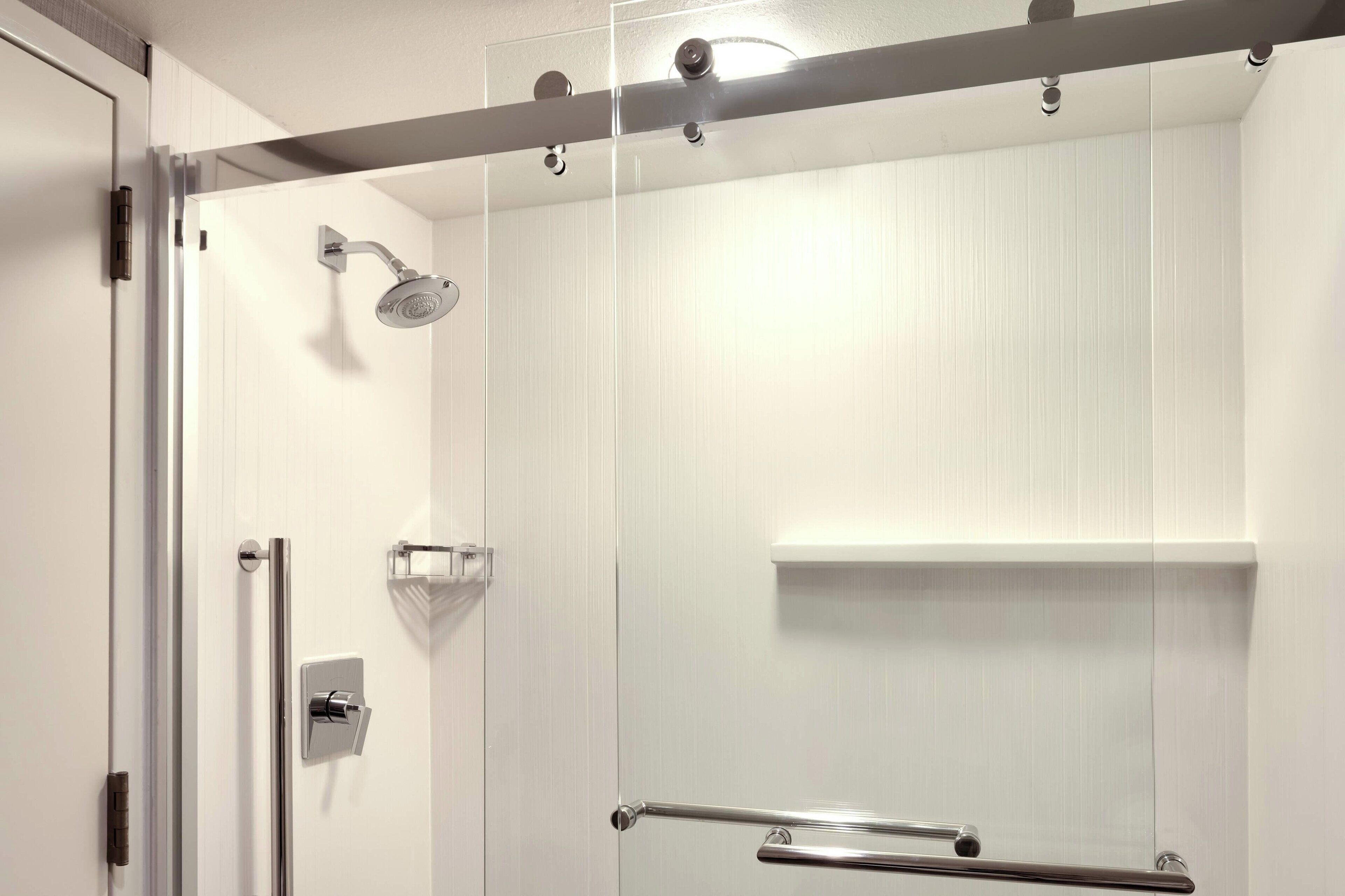 A modern shower with a glass door, a handrail, and a wall-mounted showerhead.