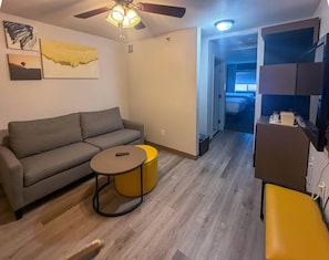 A living room with a gray sofa, a small round table, and a yellow stool. There is a ceiling fan and a painting on the wall. - Comfort Suites Albuquerque/North Journal Center (Albuquerque)
