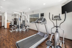 Un gimnasio con caminadora, elíptica y máquinas de pesas.