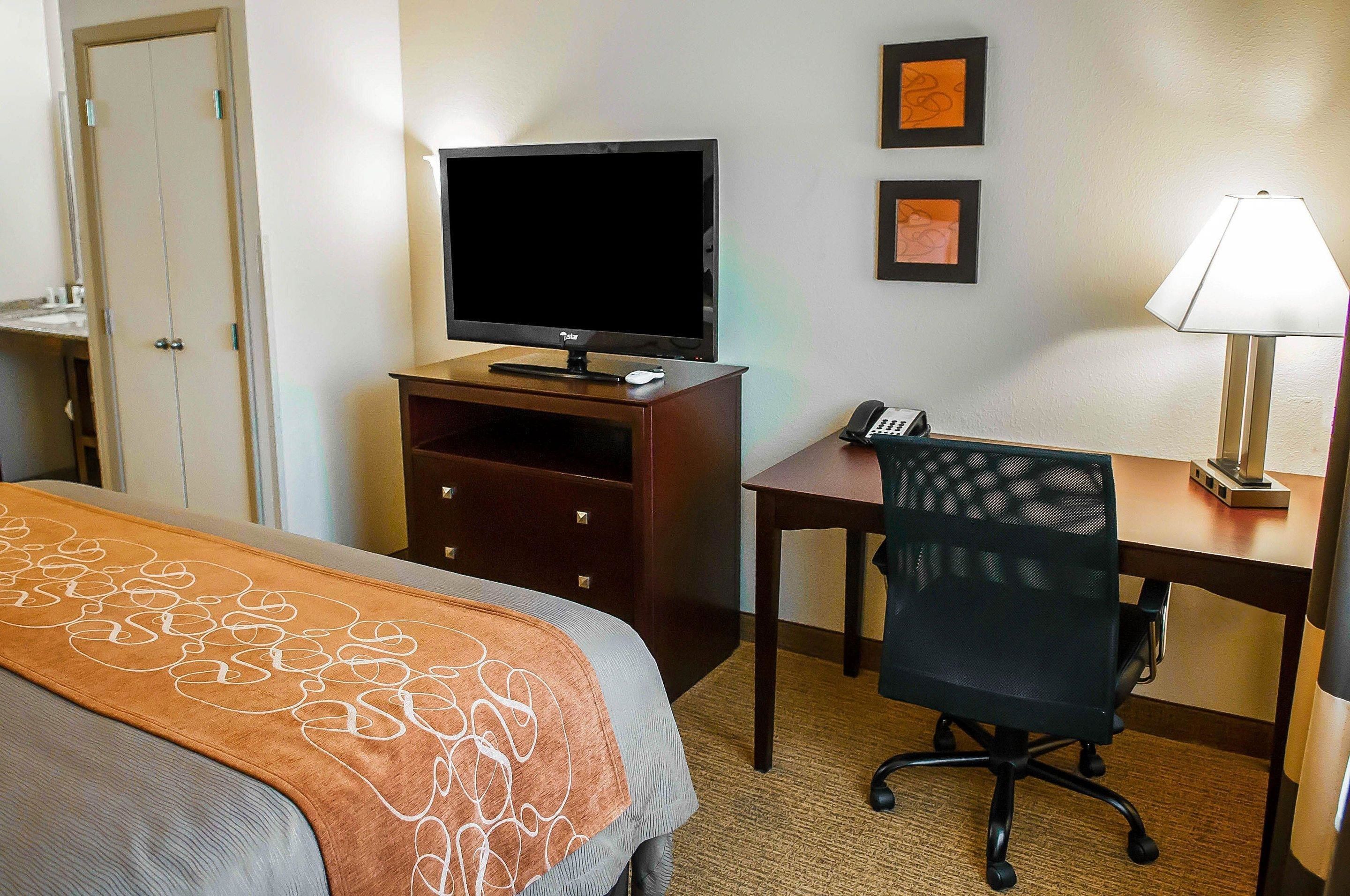 A hotel room with a bed, a desk with a computer, a television, and a lamp.