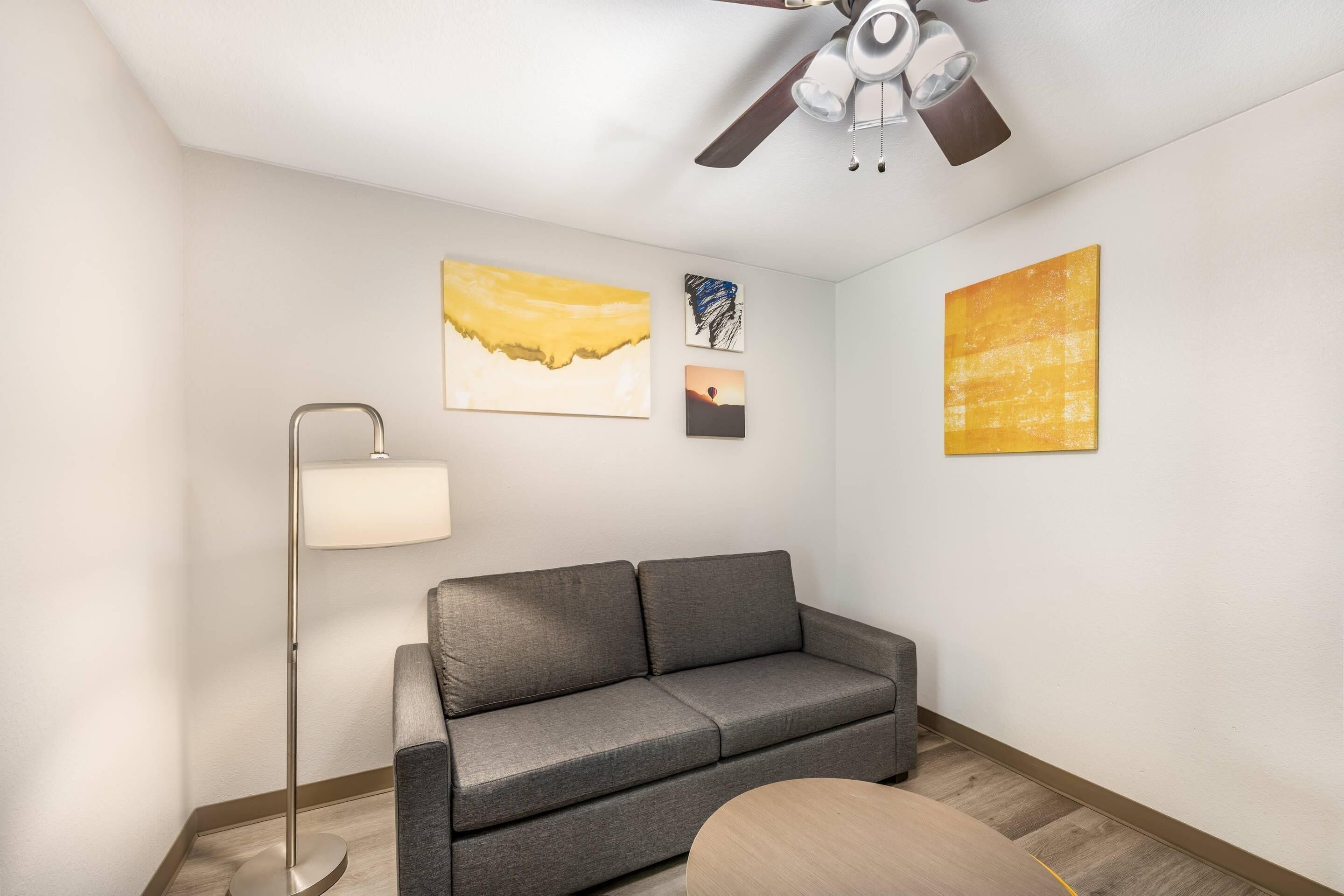 A modern living room with a grey sofa, a floor lamp, and three abstract paintings on the wall.