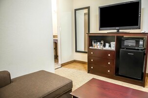 Habitación de hotel compacta con sofá, una mesita, televisor, microondas y refrigerador pequeño.