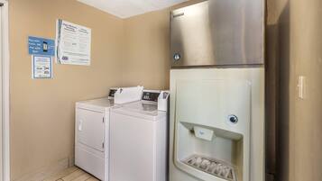 Uma lavanderia equipada com máquina de lavar e secar de carregamento frontal, geladeira em aço inoxidável e dispensador de água.