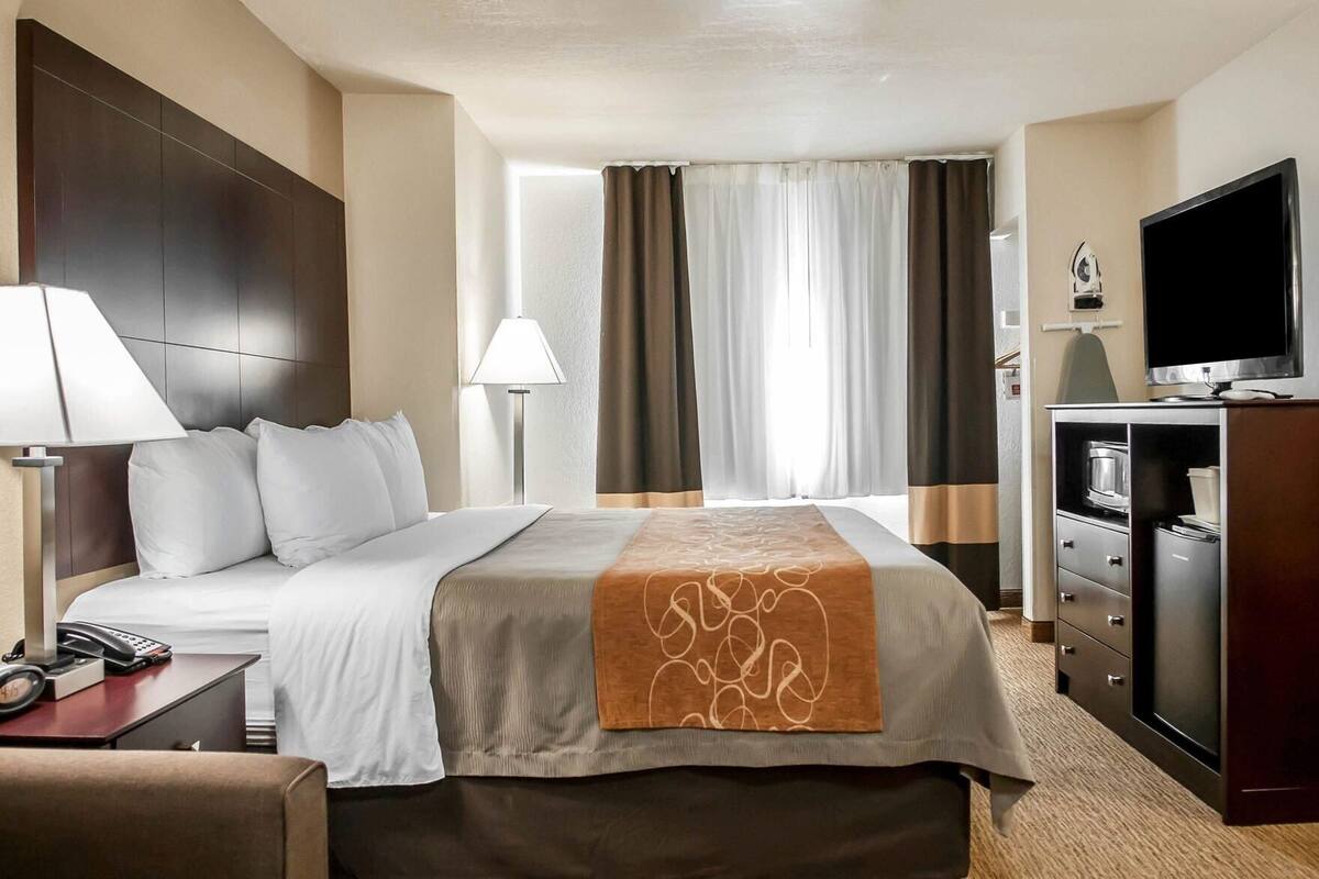 A hotel room with a bed, bedside lamp, TV, and a minibar.