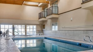 Une piscine intérieure avec un bord carrelé, un plafond en bois et un balcon doté de rampes noires.