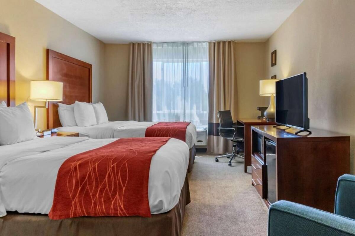 Ett hotellrum med två sängar, ett skrivbord med en tv, en stol och ett fönster med gardiner.