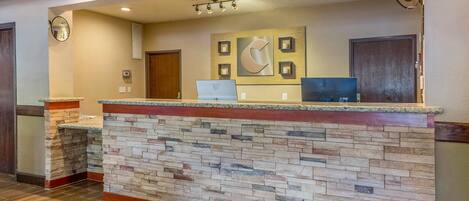 A reception area with a stone counter, a laptop, and a large wall clock.