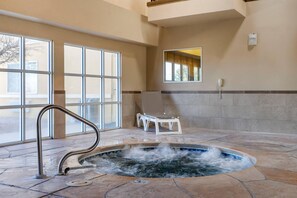 A spa area with a hot tub, a chair, and a window.