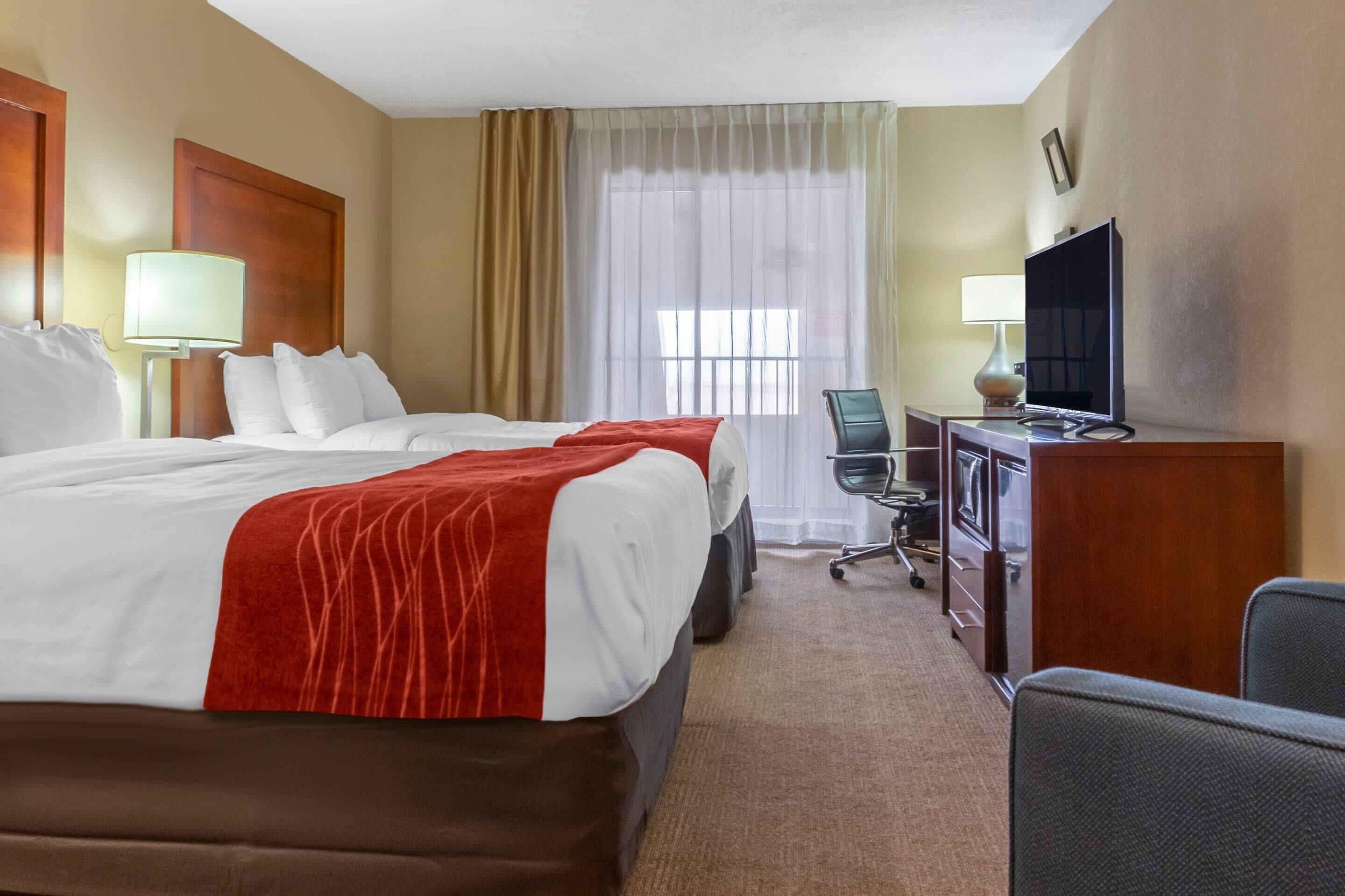A hotel room with a large bed, a desk with a computer, a chair, and a television.