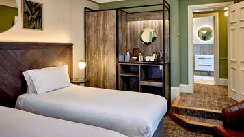 Habitación de hotel con dos camas, un armario de madera, una mesita con lámpara y un baño visible a través de una puerta abierta.