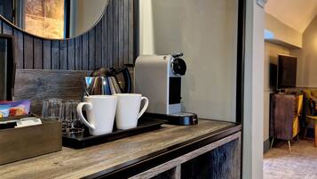 A hotel room with a wooden counter, a coffee machine, two white mugs, and a tray with glasses and a box of tissues.