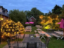 An outdoor patio area with picnic tables and chairs, surrounded by trees and a house in the background.